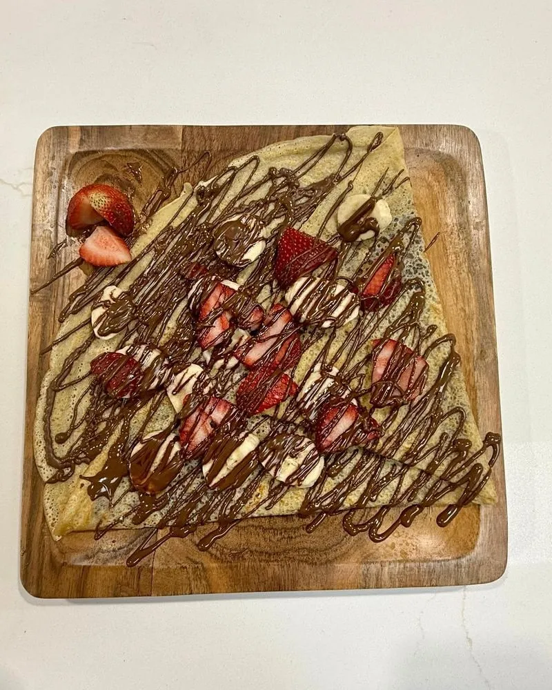 Dubai chocolate waffle topped with pistachio cream, chocolate drizzle and fresh strawberries on a wooden board