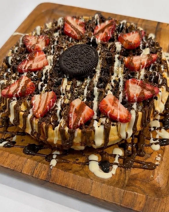 Waffle topped with fresh strawberries, cookie crumble and chocolate drizzle